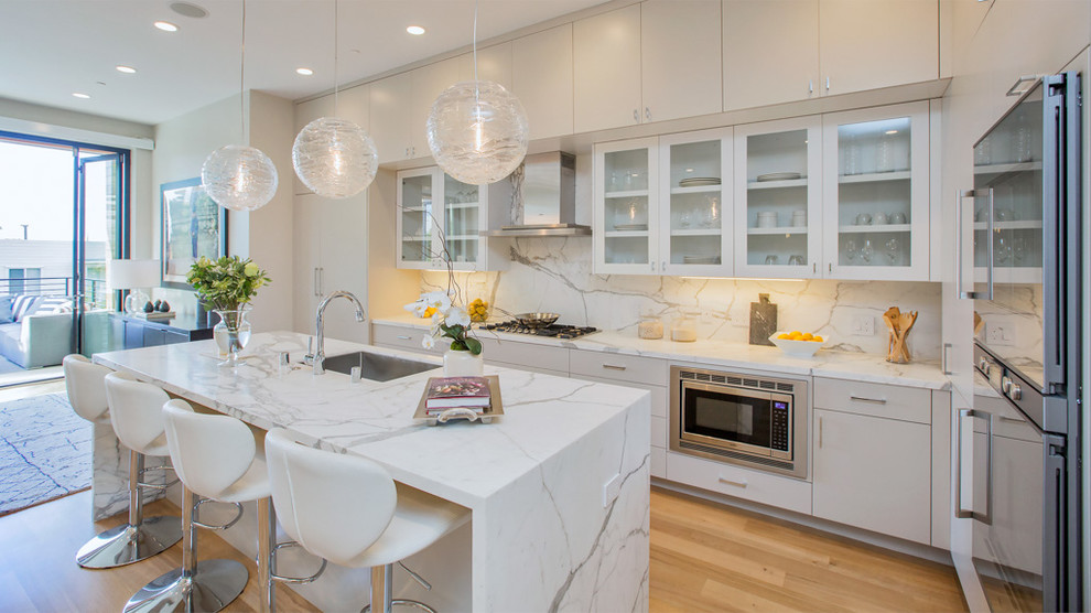 Trendy l-shaped medium tone wood floor open concept kitchen photo in San Francisco with an undermount sink, flat-panel cabinets, beige cabinets, white backsplash, stainless steel appliances, an island and marble backsplash
