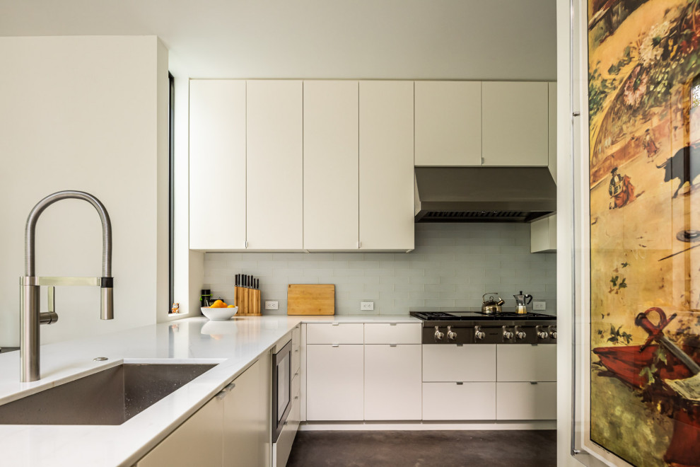 Inredning av ett modernt avskilt, stort vit vitt l-kök, med en nedsänkt diskho, släta luckor, vita skåp, marmorbänkskiva, vitt stänkskydd, rostfria vitvaror, cementgolv, en köksö och brunt golv