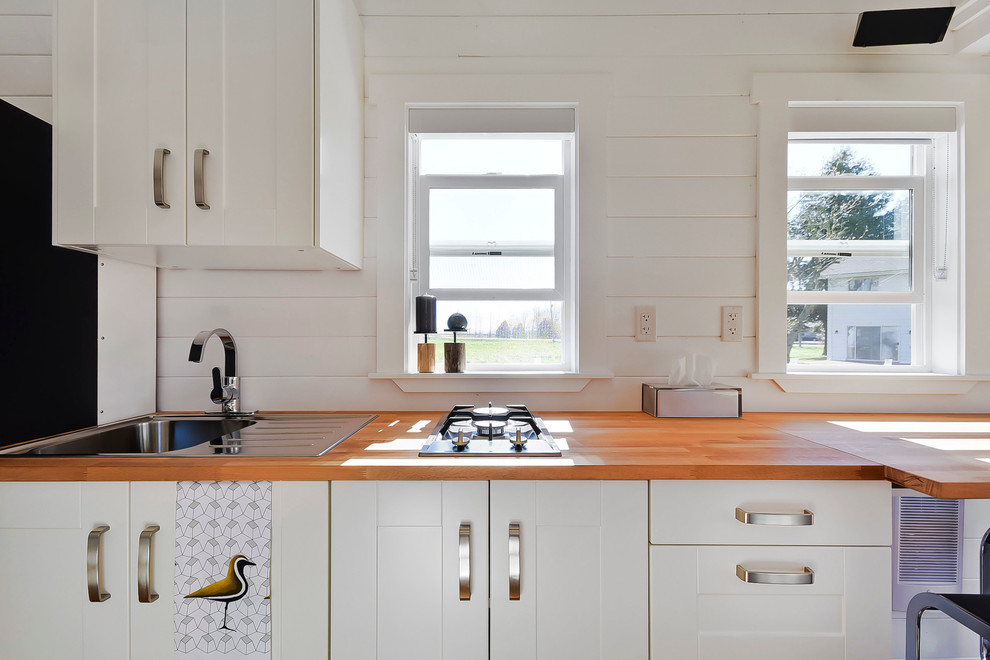 Exempel på ett litet modernt linjärt kök och matrum, med en nedsänkt diskho, släta luckor, vita skåp, träbänkskiva, svarta vitvaror, ljust trägolv och en köksö