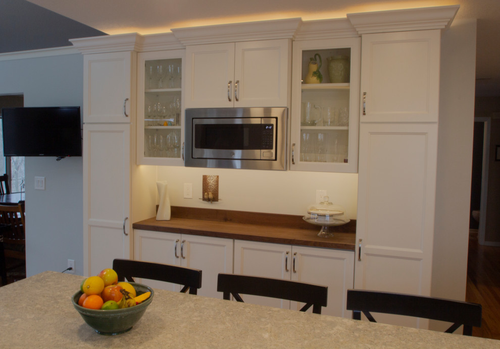Inredning av ett kök med öppen planlösning, med luckor med infälld panel, träbänkskiva, rostfria vitvaror och en köksö