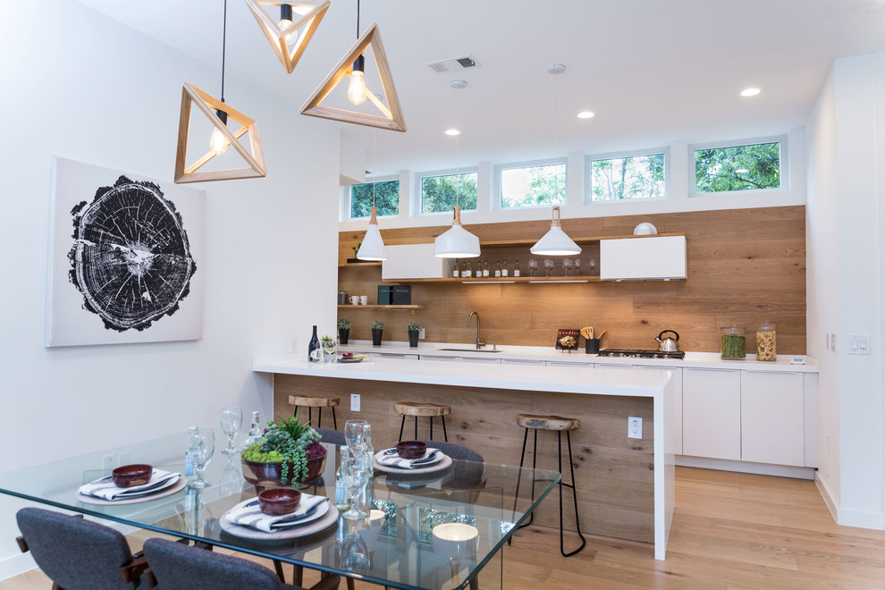 Einzeilige Moderne Wohnküche mit flächenbündigen Schrankfronten, weißen Schränken, Rückwand aus Holz, hellem Holzboden und Kücheninsel in Austin