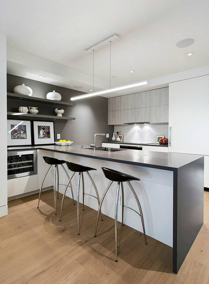 This is an example of a small contemporary galley kitchen/diner in San Francisco with a submerged sink, flat-panel cabinets, white cabinets, composite countertops, white splashback, light hardwood flooring and an island.