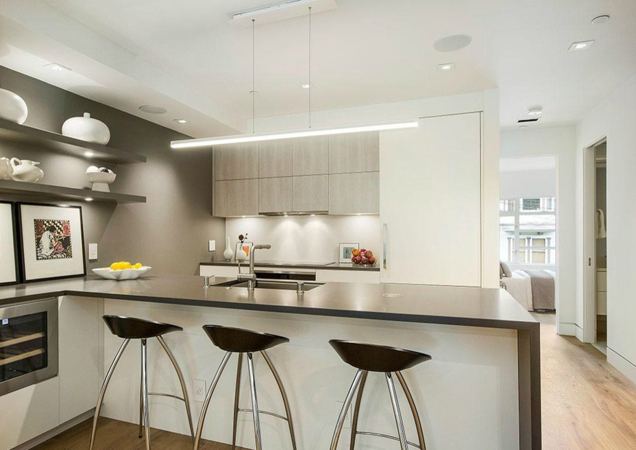 Photo of a small modern galley kitchen/diner in San Francisco with a submerged sink, flat-panel cabinets, white cabinets, composite countertops, white splashback, integrated appliances, light hardwood flooring and an island.