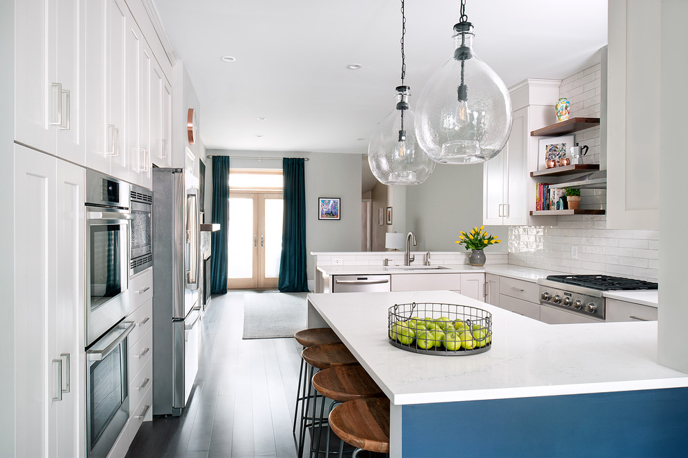 Inredning av ett modernt mellanstort vit vitt kök, med en undermonterad diskho, luckor med infälld panel, vita skåp, bänkskiva i kvarts, vitt stänkskydd, stänkskydd i keramik, rostfria vitvaror, mörkt trägolv, en halv köksö och grått golv