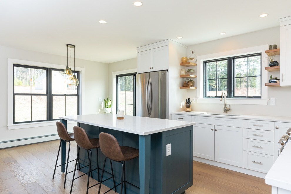 Eat-in kitchen - cottage l-shaped medium tone wood floor and brown floor eat-in kitchen idea in Portland Maine with an undermount sink, shaker cabinets, white cabinets, stainless steel appliances, an island, white countertops and beige backsplash