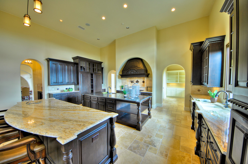 Bild på ett mycket stort medelhavsstil kök, med en dubbel diskho, luckor med upphöjd panel, skåp i mörkt trä, granitbänkskiva, beige stänkskydd, stänkskydd i kalk, integrerade vitvaror, travertin golv och flera köksöar