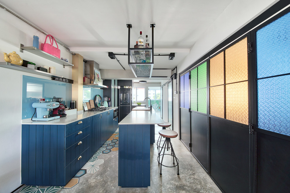 シンガポールにあるエクレクティックスタイルのおしゃれなキッチン (エプロンフロントシンク、フラットパネル扉のキャビネット、青いキャビネット、青いキッチンパネル、ガラス板のキッチンパネル、シルバーの調理設備、コンクリートの床、マルチカラーの床) の写真