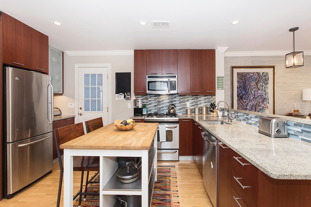 Example of a large trendy l-shaped light wood floor and brown floor kitchen design in New York with a single-bowl sink, flat-panel cabinets, dark wood cabinets, granite countertops, blue backsplash, glass tile backsplash, stainless steel appliances and a peninsula