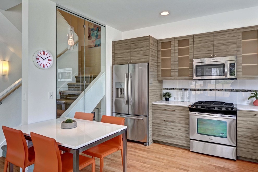 Foto di una cucina abitabile minimal con ante lisce, ante grigie, paraspruzzi bianco, elettrodomestici in acciaio inossidabile e pavimento in legno massello medio