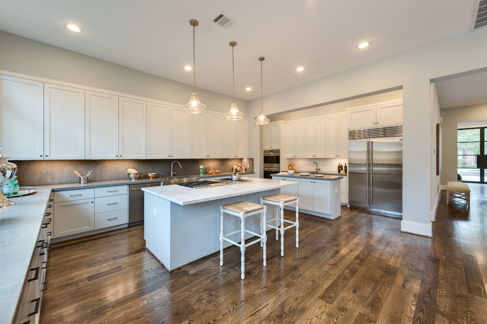 This is an example of a large traditional u-shaped open plan kitchen in Houston with a belfast sink, shaker cabinets, grey cabinets, limestone worktops, grey splashback, stone tiled splashback, stainless steel appliances, medium hardwood flooring and multiple islands.