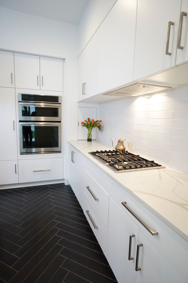 Small modern l-shaped kitchen in Richmond with a submerged sink, flat-panel cabinets, white cabinets, engineered stone countertops, white splashback, ceramic splashback, stainless steel appliances, ceramic flooring, an island, black floors and white worktops.