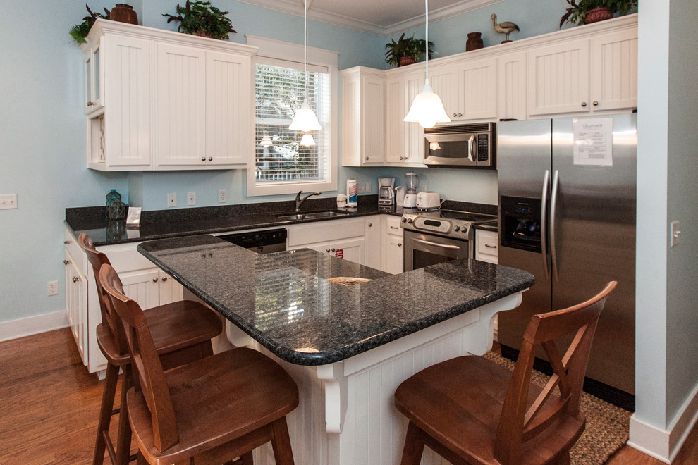 Example of a beach style l-shaped light wood floor eat-in kitchen design in Miami with an undermount sink, shaker cabinets, white cabinets, granite countertops, blue backsplash, stainless steel appliances and an island