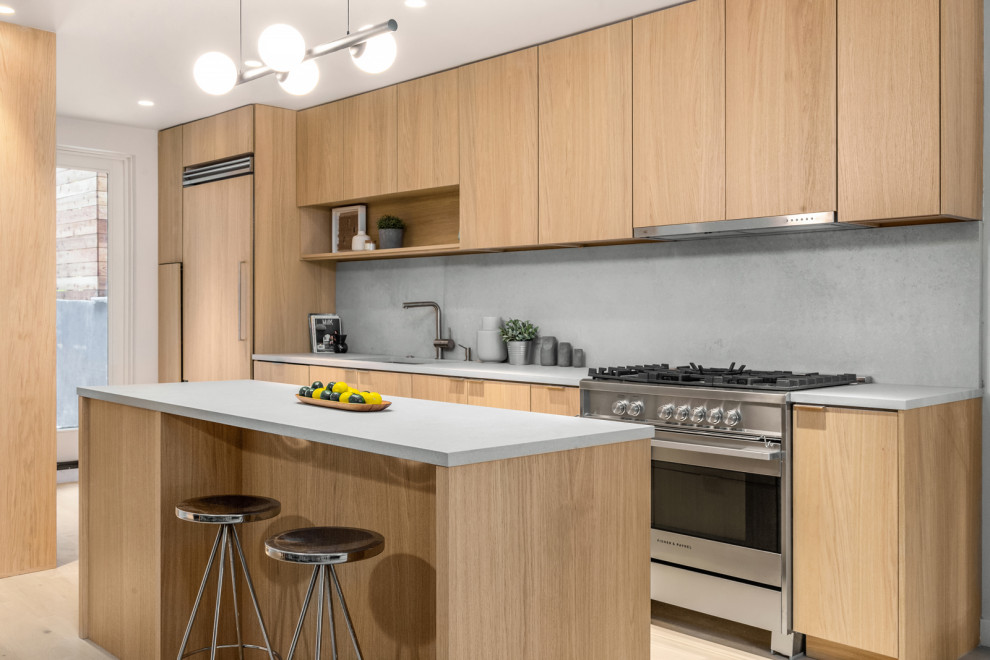 Design ideas for a contemporary galley kitchen in New York with a submerged sink, flat-panel cabinets, light wood cabinets, grey splashback, stone slab splashback, stainless steel appliances, light hardwood flooring, an island, beige floors and grey worktops.