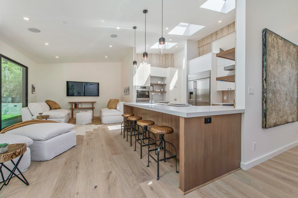 Photo of a contemporary u-shaped kitchen in San Francisco with flat-panel cabinets, white cabinets, stainless steel appliances, light hardwood flooring, a breakfast bar, beige floors and white worktops.