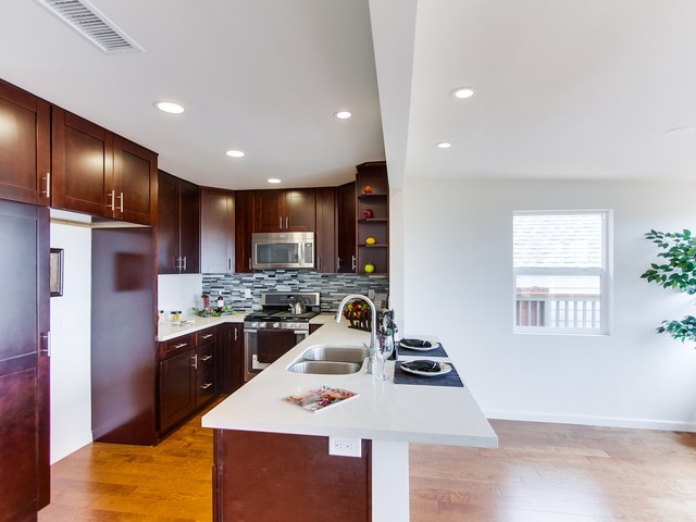 Foto på ett litet tropiskt vit kök, med en dubbel diskho, skåp i shakerstil, skåp i mörkt trä, bänkskiva i kvarts, flerfärgad stänkskydd, stänkskydd i stickkakel, rostfria vitvaror, mellanmörkt trägolv, en halv köksö och brunt golv