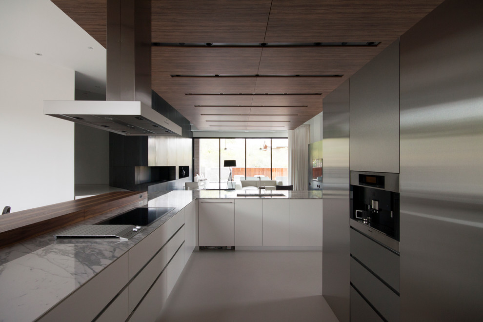 На фото: угловая кухня-гостиная в стиле модернизм с одинарной мойкой, плоскими фасадами, фасадами из нержавеющей стали, мраморной столешницей, техникой из нержавеющей стали, бетонным полом и островом с