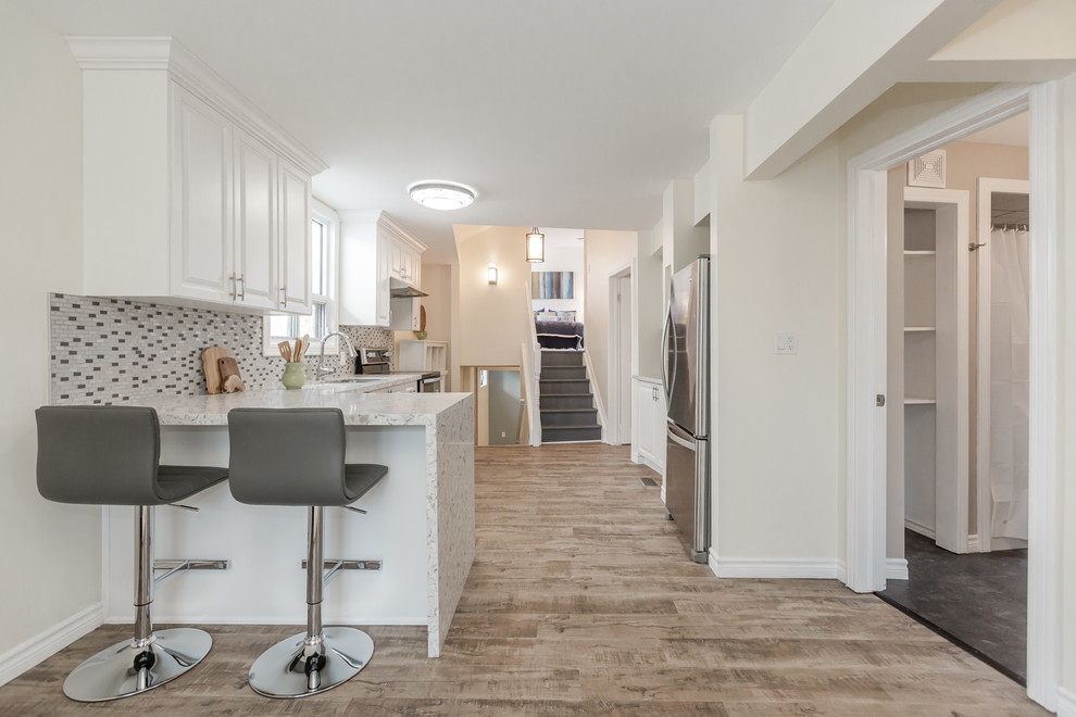 Inredning av ett modernt mellanstort kök, med en undermonterad diskho, luckor med upphöjd panel, vita skåp, marmorbänkskiva, flerfärgad stänkskydd, stänkskydd i mosaik, rostfria vitvaror, mellanmörkt trägolv, en halv köksö och brunt golv