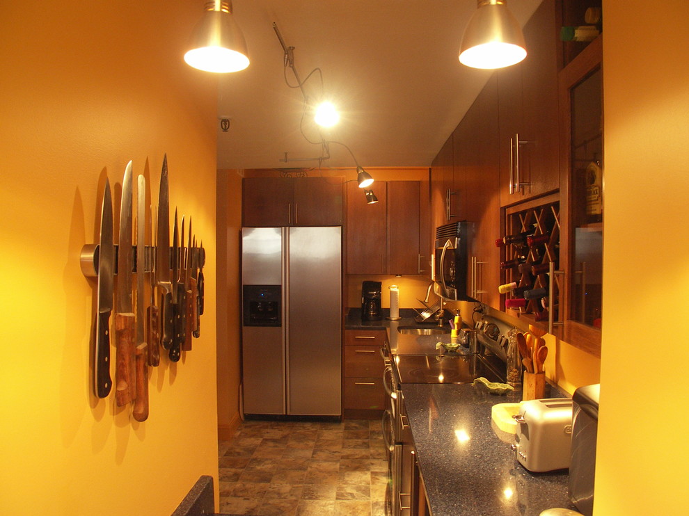 Foto på ett avskilt, litet funkis parallellkök, med en enkel diskho, släta luckor, skåp i mellenmörkt trä, bänkskiva i kvarts, orange stänkskydd, rostfria vitvaror och klinkergolv i keramik
