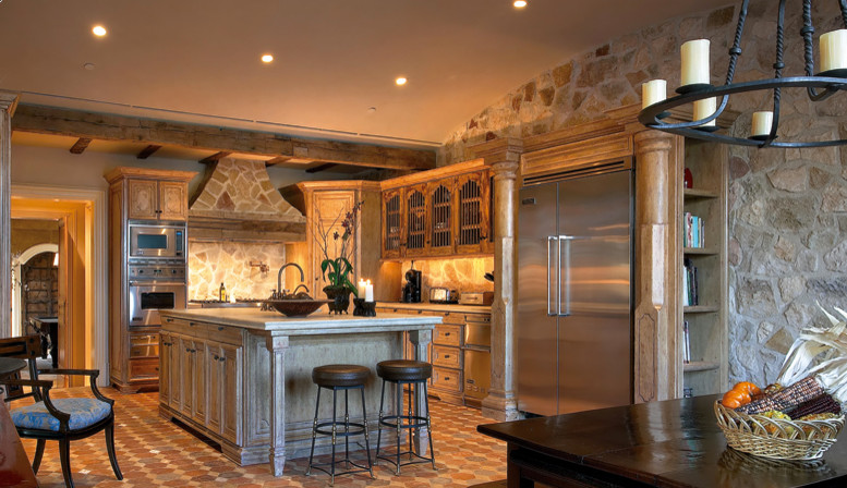Amerikansk inredning av ett kök och matrum, med luckor med profilerade fronter, skåp i ljust trä, beige stänkskydd, stänkskydd i stenkakel, rostfria vitvaror, klinkergolv i keramik och en köksö