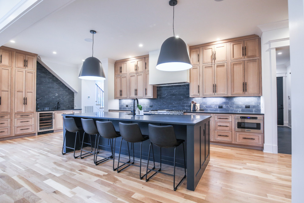 Trendy l-shaped light wood floor and beige floor kitchen photo in Nashville with an undermount sink, shaker cabinets, medium tone wood cabinets, black backsplash, stainless steel appliances, an island and black countertops