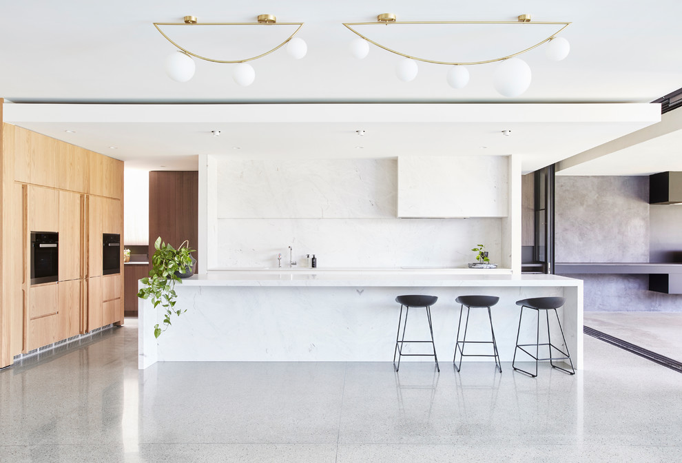 Kitchen - modern concrete floor and gray floor kitchen idea in Melbourne with flat-panel cabinets, light wood cabinets, white backsplash, paneled appliances, an island and white countertops