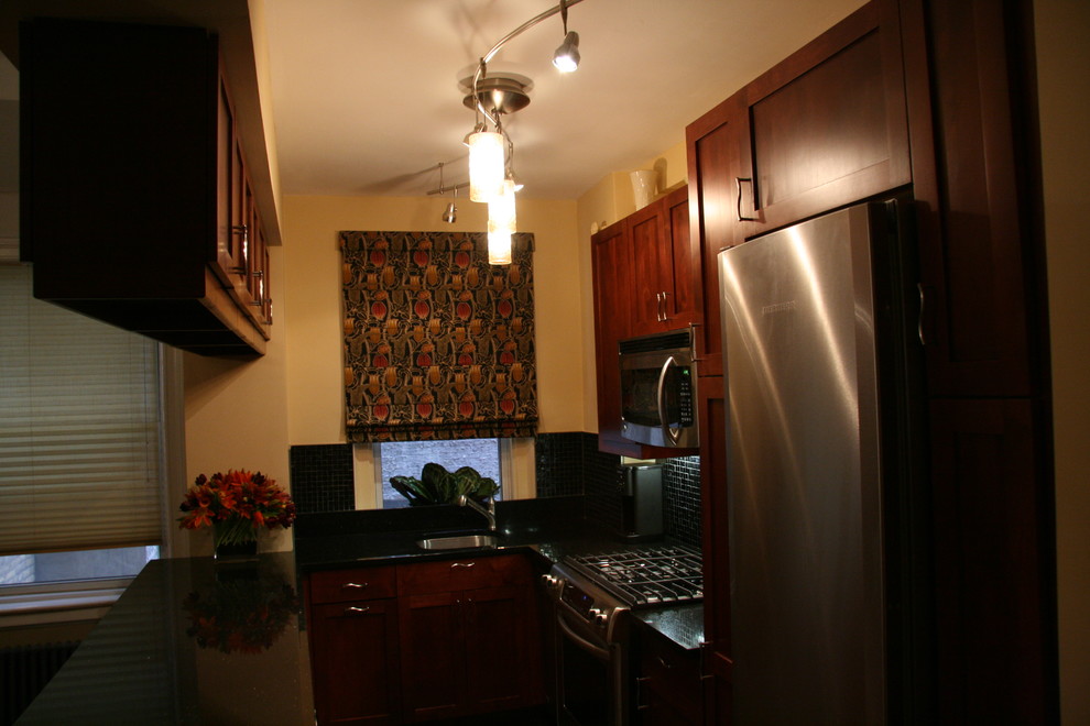 Foto di una cucina parallela tradizionale con ante in stile shaker, ante in legno scuro, paraspruzzi nero, paraspruzzi con piastrelle di vetro e elettrodomestici in acciaio inossidabile