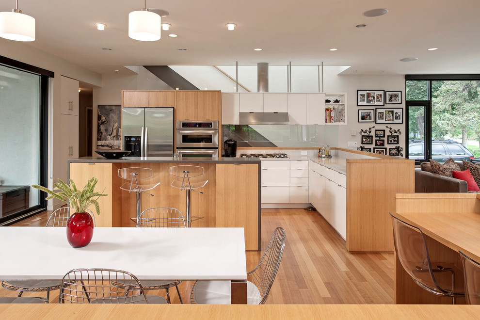 Идея дизайна: угловая кухня-гостиная в современном стиле с плоскими фасадами, белыми фасадами, техникой из нержавеющей стали, паркетным полом среднего тона и островом