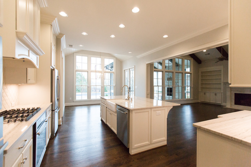 Inspiration for a large transitional l-shaped dark wood floor and brown floor open concept kitchen remodel in Birmingham with a farmhouse sink, recessed-panel cabinets, white cabinets, quartzite countertops, white backsplash, ceramic backsplash, stainless steel appliances, an island and white countertops