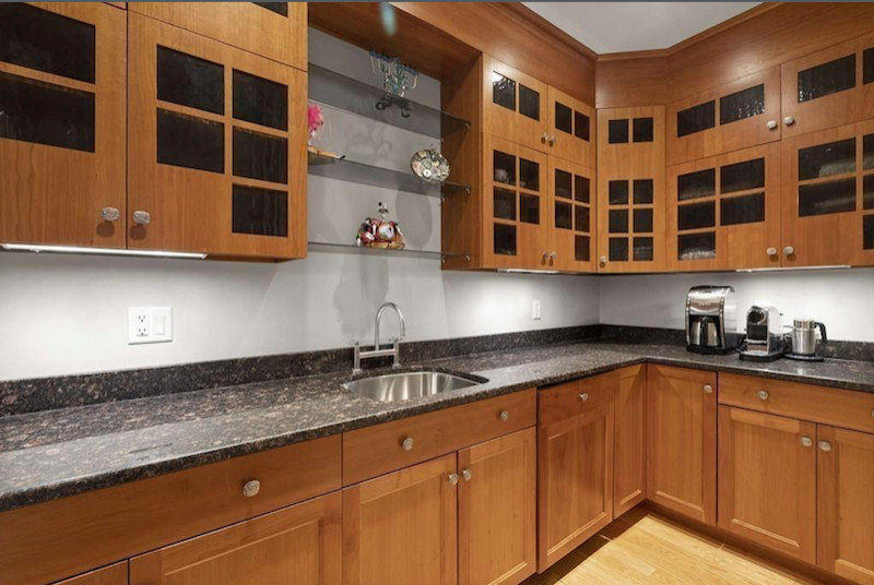 Amerikansk inredning av ett stort svart svart l-kök, med en nedsänkt diskho, luckor med infälld panel, skåp i ljust trä, granitbänkskiva, svart stänkskydd, rostfria vitvaror och ljust trägolv