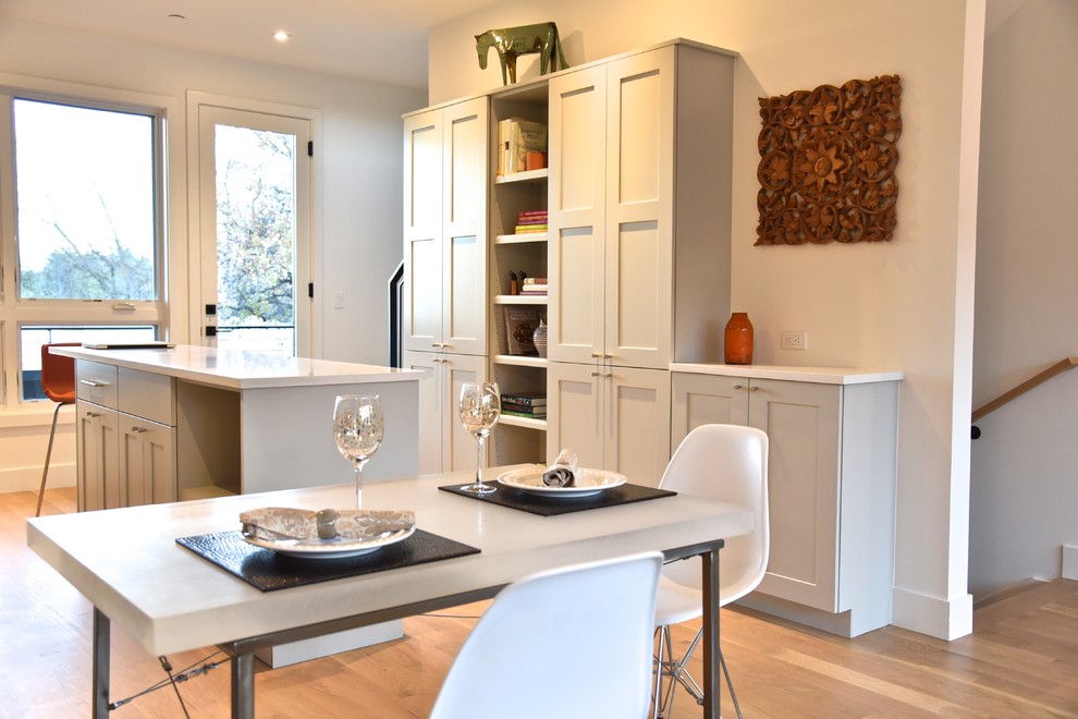 Bild på ett litet funkis kök, med en enkel diskho, skåp i shakerstil, grå skåp, bänkskiva i kvarts, vitt stänkskydd, stänkskydd i porslinskakel, rostfria vitvaror, ljust trägolv, en köksö och brunt golv
