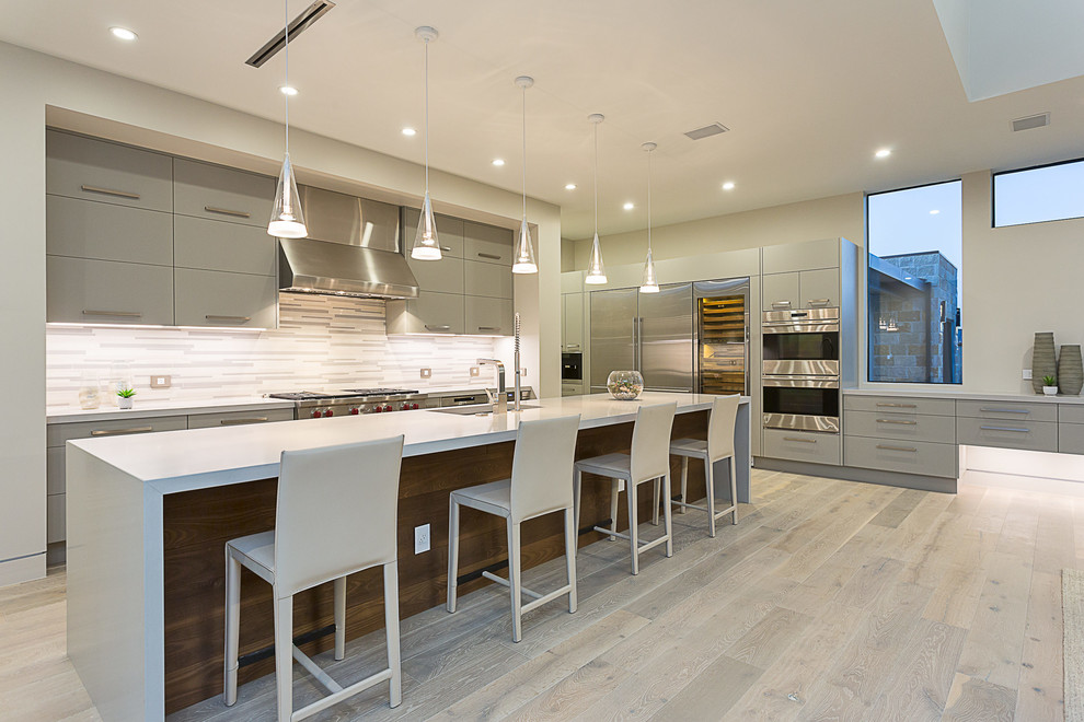 Moderne Küche in L-Form mit Unterbauwaschbecken, flächenbündigen Schrankfronten, grauen Schränken, Küchenrückwand in Weiß, Küchengeräten aus Edelstahl, hellem Holzboden und Kücheninsel in Austin