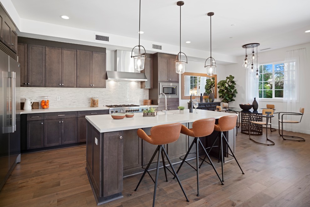 Inspiration for a transitional medium tone wood floor and brown floor eat-in kitchen remodel in Orange County with an undermount sink, shaker cabinets, dark wood cabinets, white backsplash, matchstick tile backsplash, stainless steel appliances, an island and white countertops