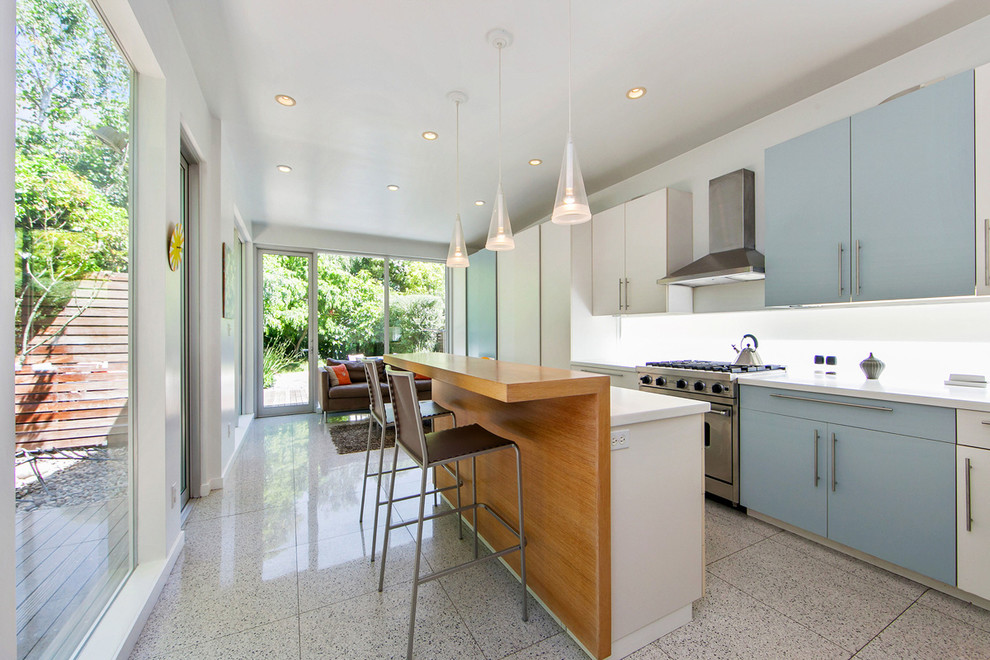 Cette photo montre une cuisine linéaire tendance avec un placard à porte plane, des portes de placard bleues, une crédence blanche, un électroménager en acier inoxydable et îlot.