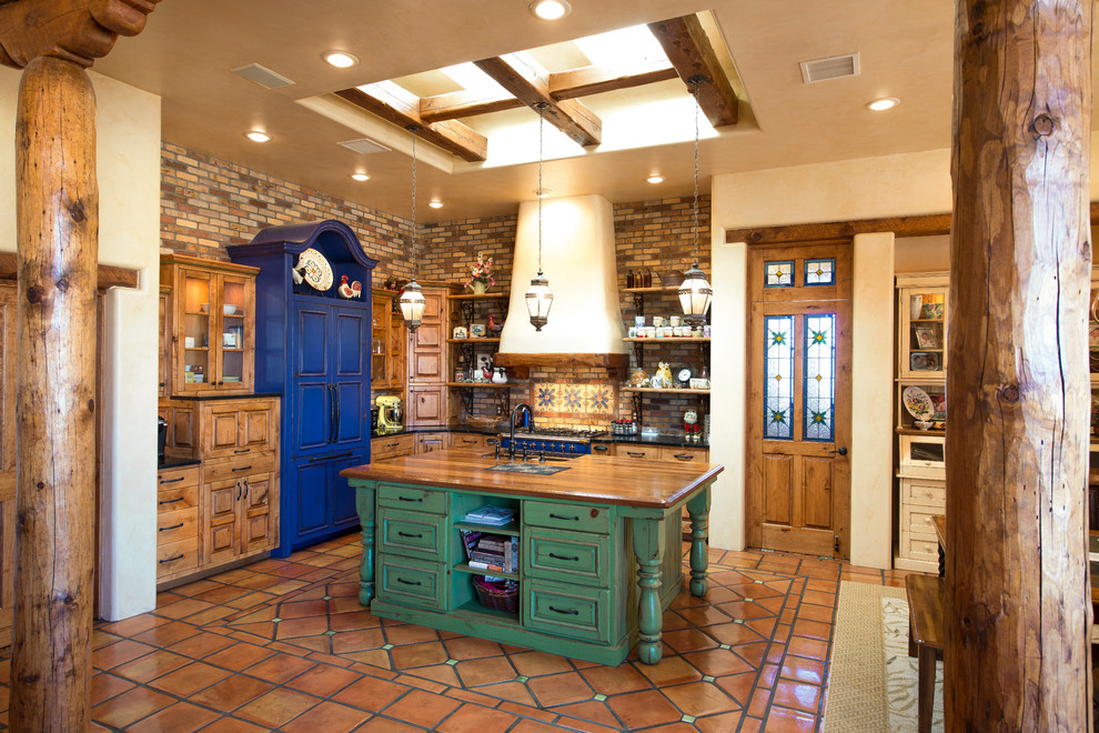 オースティンにあるサンタフェスタイルのおしゃれなキッチン (レイズドパネル扉のキャビネット、中間色木目調キャビネット、茶色いキッチンパネル、パネルと同色の調理設備、テラコッタタイルの床) の写真