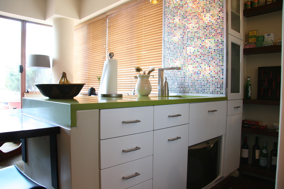 This is an example of a small contemporary galley kitchen in New York with flat-panel cabinets, white cabinets, multi-coloured splashback and glass tiled splashback.