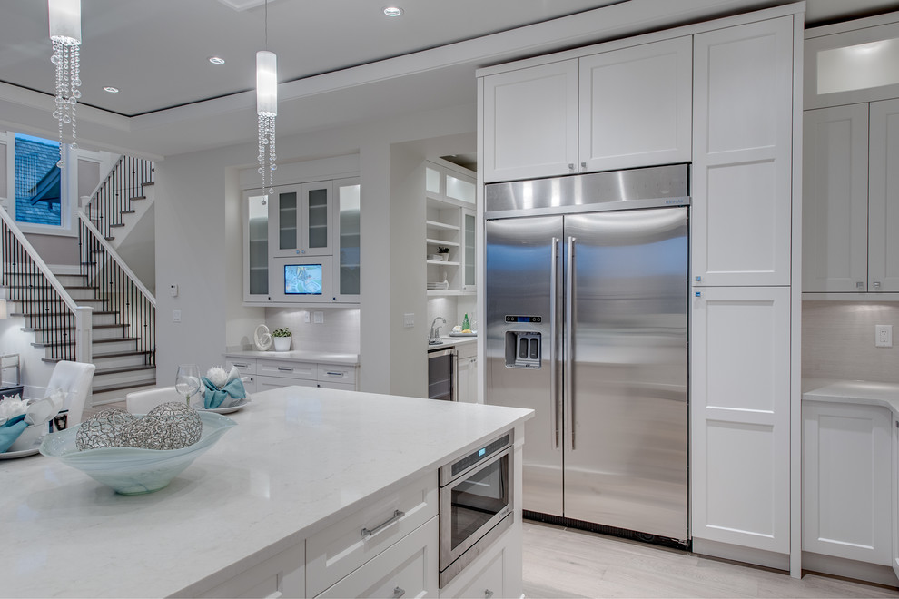 Medium sized classic u-shaped open plan kitchen in Vancouver with white cabinets, recessed-panel cabinets, white splashback, stainless steel appliances, light hardwood flooring, an island and a belfast sink.