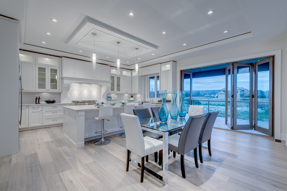 This is an example of a medium sized classic u-shaped open plan kitchen in Vancouver with recessed-panel cabinets, white cabinets, white splashback, stainless steel appliances, light hardwood flooring, an island, a belfast sink and beige floors.