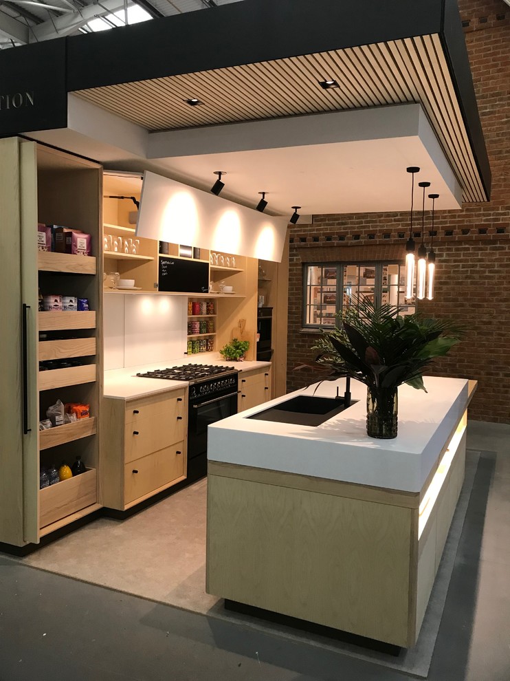 Medium sized scandinavian galley open plan kitchen in Wiltshire with an integrated sink, flat-panel cabinets, light wood cabinets, composite countertops, white splashback, glass sheet splashback, black appliances, concrete flooring, an island, grey floors and white worktops.