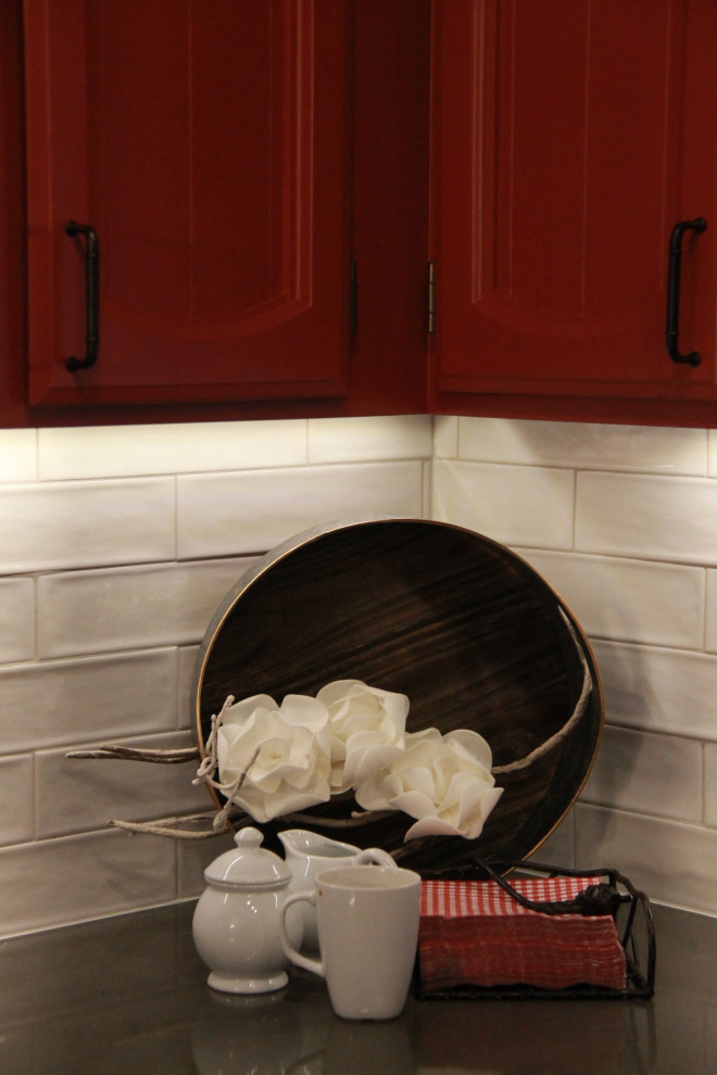 Inredning av ett klassiskt litet brun brunt kök, med en undermonterad diskho, luckor med upphöjd panel, röda skåp, bänkskiva i kvartsit, vitt stänkskydd, stänkskydd i porslinskakel, rostfria vitvaror, laminatgolv, en halv köksö och brunt golv