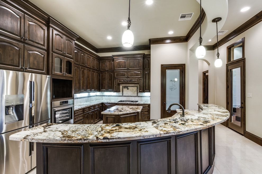Large classic l-shaped open plan kitchen in Houston with a submerged sink, raised-panel cabinets, dark wood cabinets, granite worktops, multi-coloured splashback, stone tiled splashback, stainless steel appliances, limestone flooring, multiple islands and beige floors.