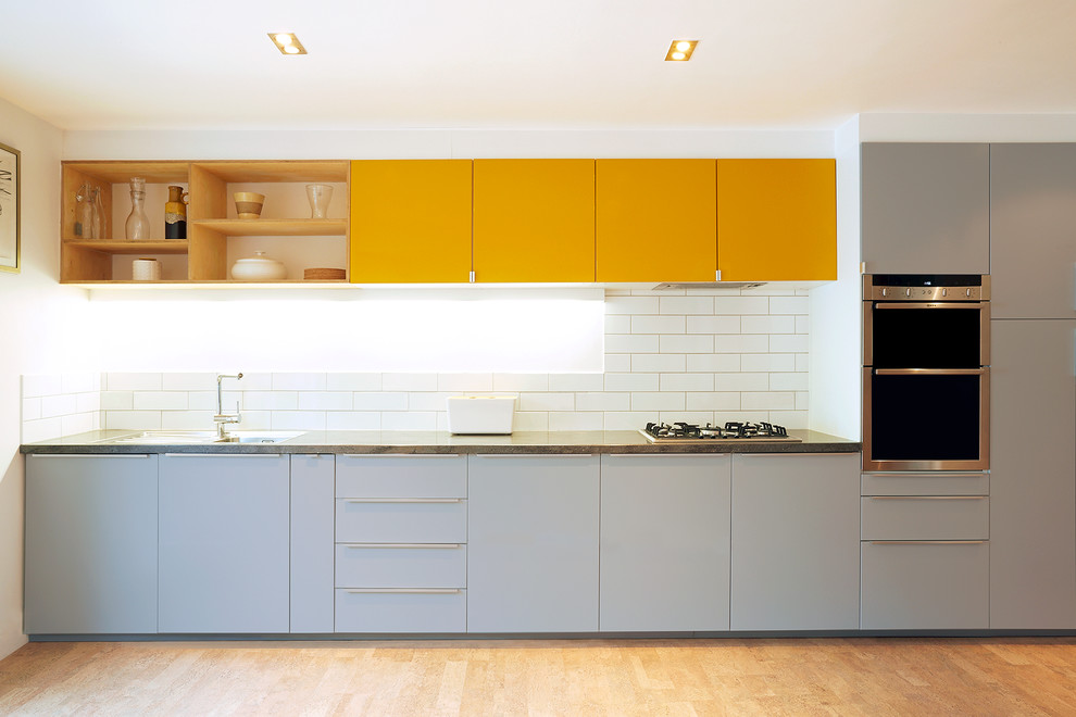 Идея дизайна: прямая кухня-гостиная среднего размера в современном стиле с плоскими фасадами, желтыми фасадами, столешницей из бетона, белым фартуком, фартуком из керамогранитной плитки и техникой из нержавеющей стали