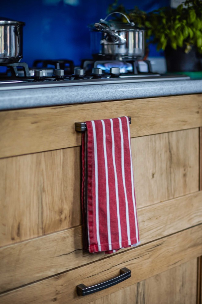 Cette image montre une cuisine victorienne en bois brun fermée avec une crédence bleue, une crédence en feuille de verre et un électroménager en acier inoxydable.