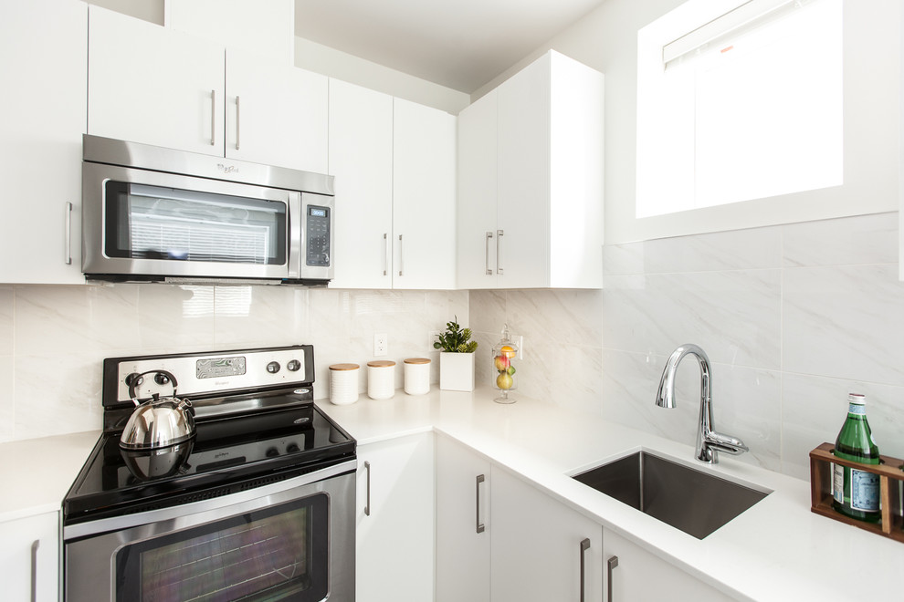 Cette image montre une cuisine design en L avec un évier encastré, un placard à porte plane, des portes de placard blanches, une crédence blanche et un électroménager en acier inoxydable.