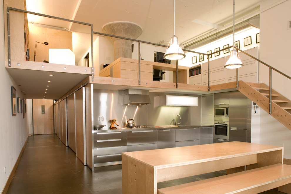 Foto på ett mellanstort industriellt kök, med släta luckor, skåp i rostfritt stål, stänkskydd med metallisk yta, stänkskydd i metallkakel, rostfria vitvaror och betonggolv