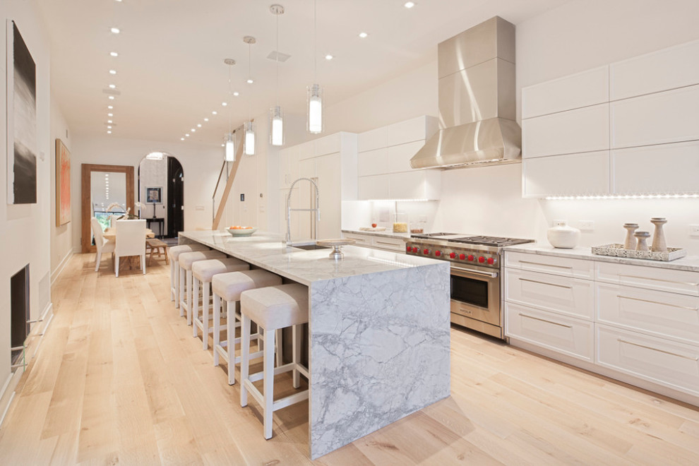 Cette image montre une cuisine design avec des portes de placard blanches, un électroménager en acier inoxydable et îlot.