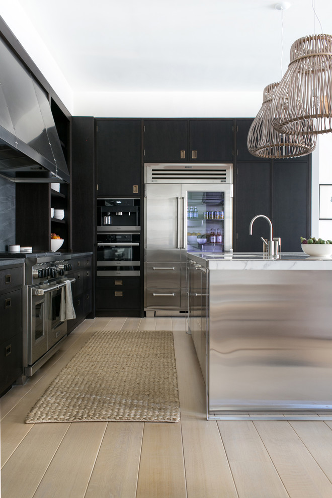 Photo of a large traditional l-shaped open plan kitchen in New York with a submerged sink, dark wood cabinets, marble worktops, black splashback, limestone splashback, stainless steel appliances, light hardwood flooring and an island.