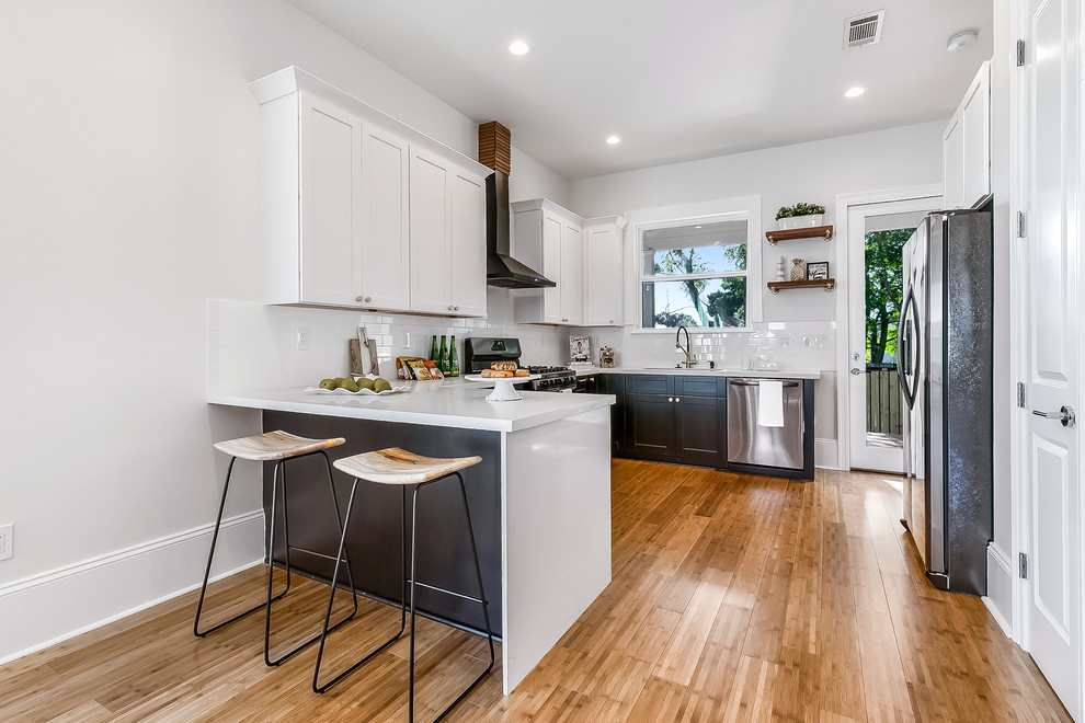 Inspiration for a mid-sized 1950s u-shaped bamboo floor and brown floor open concept kitchen remodel in New Orleans with an undermount sink, shaker cabinets, white cabinets, solid surface countertops, white backsplash, subway tile backsplash, stainless steel appliances, no island and white countertops