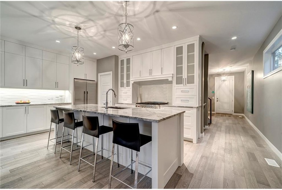 Eat-in kitchen - mid-sized transitional l-shaped light wood floor eat-in kitchen idea in Calgary with shaker cabinets, white cabinets, an island, marble countertops, gray backsplash, an undermount sink, stone tile backsplash and stainless steel appliances