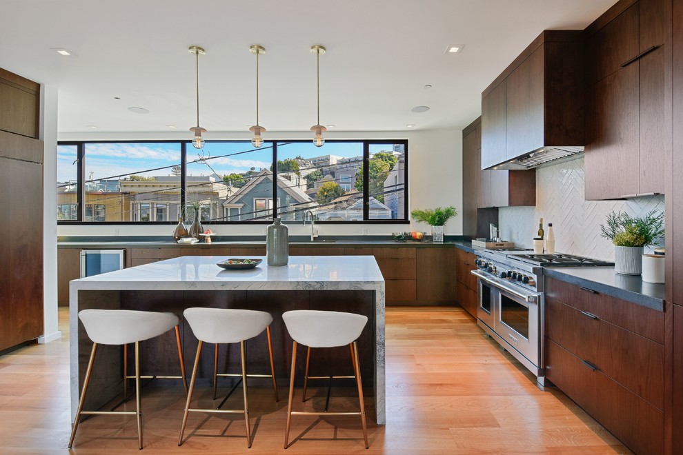 Contemporary u-shaped kitchen in San Francisco with flat-panel cabinets, dark wood cabinets, white splashback, medium hardwood flooring, an island, brown floors and white worktops.