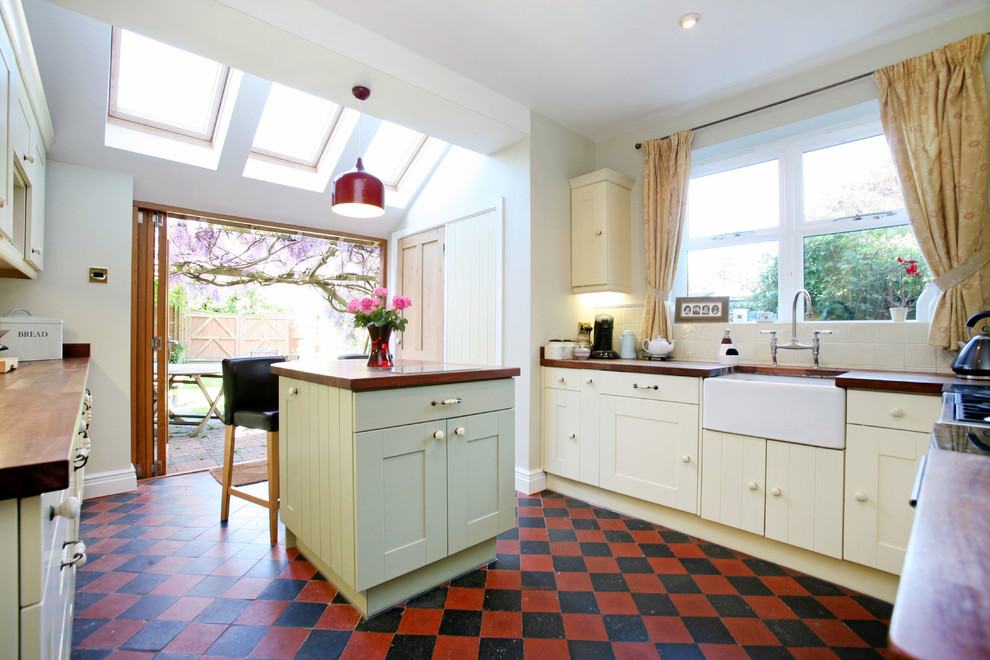 Geschlossene Klassische Küche mit Landhausspüle, gelben Schränken, Arbeitsplatte aus Holz, buntem Boden und brauner Arbeitsplatte in London